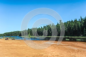 People driving ATV quads on sand beach of Foyross Lake. Foy, Sudbury, Ontario, Canada.