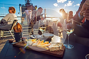 People eating cheese and drinking wine at rooftop restaurant at sunset time.