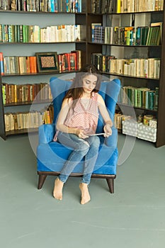 People, education and technology concept - cute young female student using a tablet computer in a library