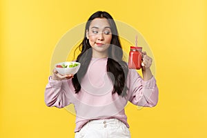 People emotions, healthy lifestyle and food concept. Curious cute asian girl looking at smoothie, holding salad and