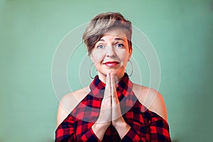 People and emotions - a portrait of smiling young woman with short hair keeps palms together and pleads about something