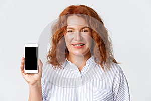 People, emotions and technology concept. Close-up of pleased pretty middle-aged woman, showing smartphone screen and