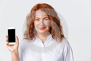 People, emotions and technology concept. Close-up of pretty middle-aged woman, mother with red hair showing smartphone
