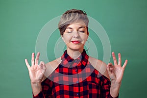 People,emotions and yoga concept -a portrait of woman relaxing and smiling with eyes closed doing meditation gesture with fingers