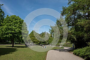 People enjoy leisure activities and small path surrounded with tranquil, shady and natural atmosphere of Zoo Park in DÃ¼sseldorf.