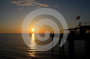 People enjoy sunset over Black Sea horizon at pier with flag Batumi Georgia