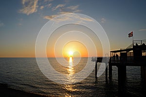 People enjoy sunset over Black Sea horizon at pier with flag Batumi Georgia