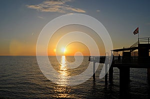 People enjoy sunset over Black Sea horizon at pier with flag Batumi Georgia