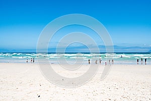 People enjoying water of Atlantic Ocean and wide white beach in Kalk Bay, South Africa.