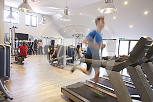 People exercising in a gym, blurred man runs in foreground