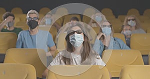 People in face masks watching 3d film in cinema on coronavirus quarantine. Portrait of men and women in movie theater on