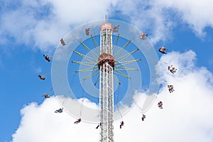 People in a fairground carousel swinging high up in the air against a cloudy blu sky.