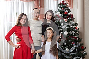 People family, christmas and adoption concept - happy mother, father and children hugging near a Christmas tree at home