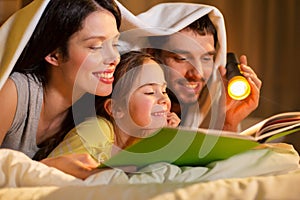 Happy family reading book in bed at night at home