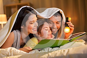 Happy family reading book in bed at night at home