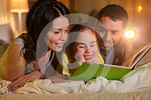 Happy family reading book in bed at night at home