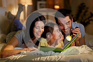 Happy family reading book in bed at night at home