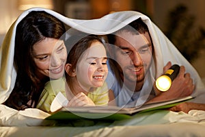 Happy family reading book in bed at night at home