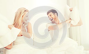 Happy couple having pillow fight in bed at home