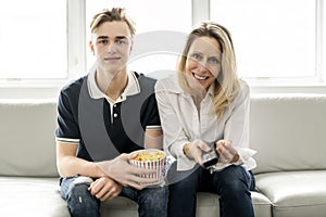 A people and family happy teen boy with mother on sofa at home listening TV