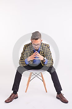 People, fashion and beauty concept - handsome young confident man sitting on the chair, isolated on white background