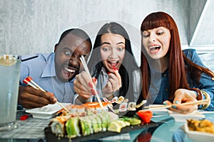 People, food, fun, sushi meal. Close up shot of excited hungry funny three multiethnical friends, having fun at cafe