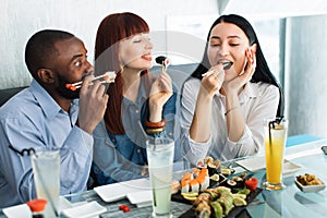 People, food, fun, sushi meal. Close up shot of excited hungry funny three multiethnical friends, having fun at cafe