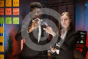 People in formal wear using adhesive notes and writing while standing behind the glass wall