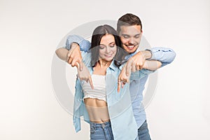 People and gesture concept - young pretty woman and handsome man pointing down over white background