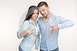 People and gesture concept - young pretty woman and handsome man pointing down over white background