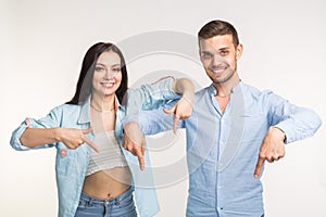 People and gesture concept - young pretty woman and handsome man pointing down over white background