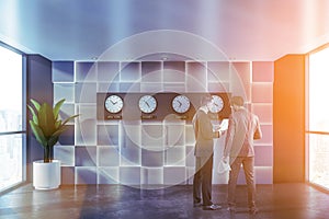 People in gray office lobby with clocks