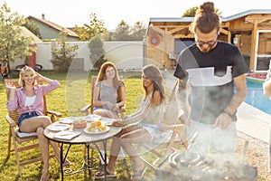 People grilling meat and having fun at poolside backyard barbecue party