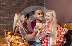 People Group Eating Fast Food Burgers Sitting At Wooden Table In Cafe