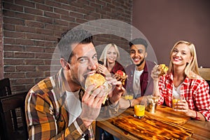 People Group Eating Fast Food Burgers Sitting At Wooden Table In Cafe