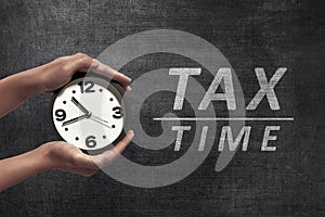 People hand holding black alarm clock beside Tax time announcement