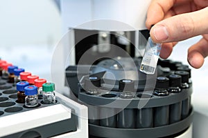People hand holding a test tube vial sets for analysis in the gas liquid chromatograph. Laboratory assistant inserting laboratory