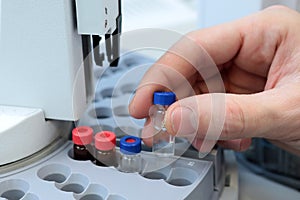 People hand holding a test tube vial sets for analysis in the gas liquid chromatograph. Laboratory assistant inserting laboratory