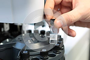 People hand holding a test tube vial sets for analysis in the gas liquid chromatograph. Laboratory assistant inserting laboratory