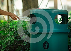 People hand throwing empty water bottle in recycle bin at park. Green plastic recycle bin. Man discard bottle in trash bin. Waste photo