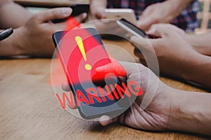 people hand using mobile smart phone with virtual malware attack warning graphic icon on desk