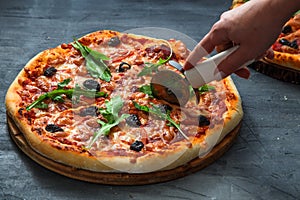 People Hands cutting homemade pizza with tomato, salumi, olives and arugula