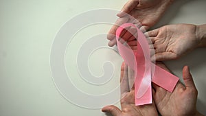 People hands showing pink ribbon to camera, breast cancer prevention campaign