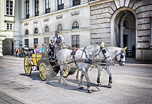 People have a ride in the fiaker and pass the Hofburg in Vienna