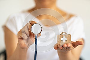 People and Healthcare concept. Closeup of woman hand holding stethoscope with wooden diecut bag with medical cross logo