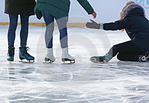 People help to get up after a fall skating on the ice rink