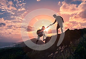 People helping each other hike up a mountain at sunrise. Giving a helping hand.