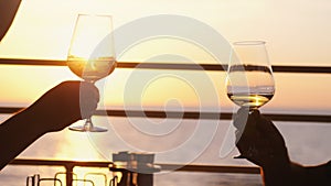 People holding glass of wine, making a toast over sunset. Friends drinking white wine, toasting. Clink. Party outdoors