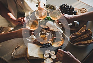 People holding glasses with orange or rose wine over snacks