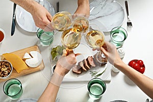 People holding glasses of white wine over table with tasty snacks